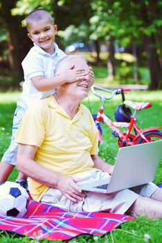 happy elderly senior grandfather and child in park using laptop computer