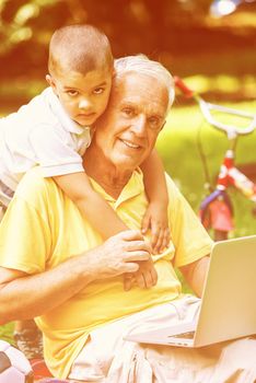 happy elderly senior grandfather and child in park using laptop computer