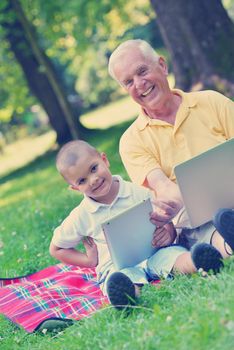 happy elderly senior grandfather and child in park using laptop computer