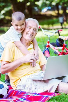 happy elderly senior grandfather and child in park using laptop computer