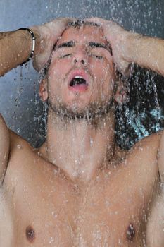 young good looking and attractive man with muscular body wet taking showe in bath with black tiles in background