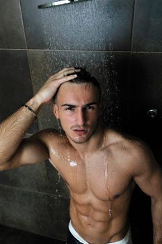 young good looking and attractive man with muscular body wet taking showe in bath with black tiles in background