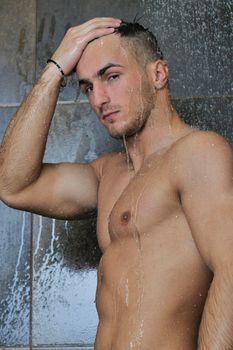 young good looking and attractive man with muscular body wet taking showe in bath with black tiles in background