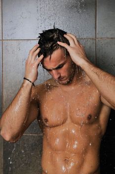 young good looking and attractive man with muscular body wet taking showe in bath with black tiles in background