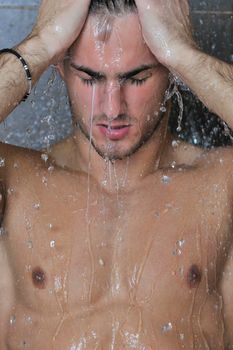 young good looking and attractive man with muscular body wet taking showe in bath with black tiles in background