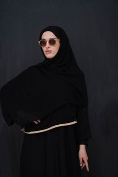 Young muslim in traditional clothes or abaya and sunglasses posing in front of black chalkboard. Arab woman representing modern arabic lifestyle, islamic  fashion and Ramadan kareem concept