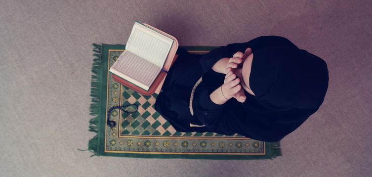 Middle eastern woman praying and reading the holy Quran (public item of all muslims). Education concept of Muslim woman studying The holy Quran at home or mosque in ramadan month.