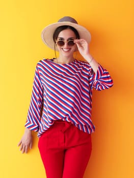 Portrait of young woman wearing sunglasses and hat over a yellow background. Female model posing in the studio. Concept of fashion