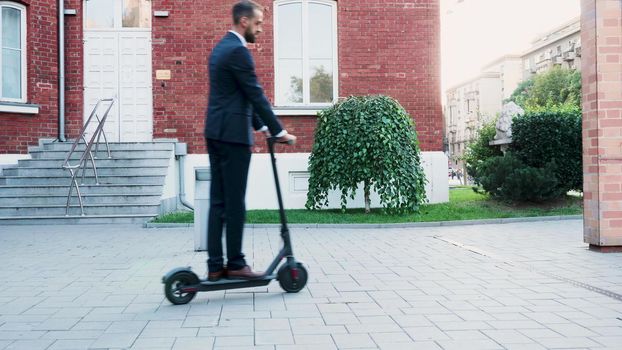 Businessman in diplomatic suit riding on electric scooter in front of startup office company. Entrepreneur man going to business meeting. Concept of eco-friendly transportation