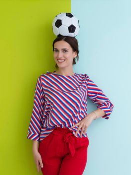 Portrait of young European woman holding soccer ball on her head. Happy girl, football fan or player isolated on green and blue background. Sport, play football, health, healthy lifestyle concept