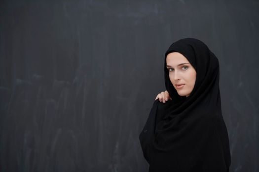 Modern young muslim woman in black abaya. Arab girl wearing traditional clothes and posing in front of black chalkboard. Representing modern and rich arabic lifestyle