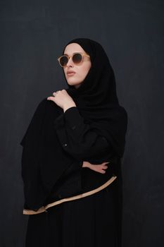 Young muslim in traditional clothes or abaya and sunglasses posing in front of black chalkboard. Arab woman representing modern arabic lifestyle, islamic  fashion and Ramadan kareem concept