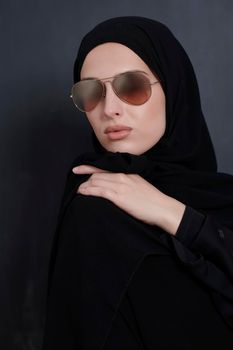 Young muslim businesswoman in traditional clothes or abaya and sunglasses posing in front of black chalkboard. Arab woman representing modern arabic lifestyle, islamic  fashion and Ramadan kareem concept