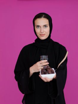 Modern muslim woman in abaya holding a date fruit and glass of water in front of her. Concept celebration of iftar time, end of fasting, in ramadan holy month