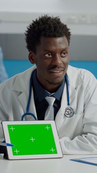 Young doctor with green screen technology on tablet for healthcare consultation at desk with old woman in cabinet. Medic using horizontal isolated template of mockup and chroma key for patient