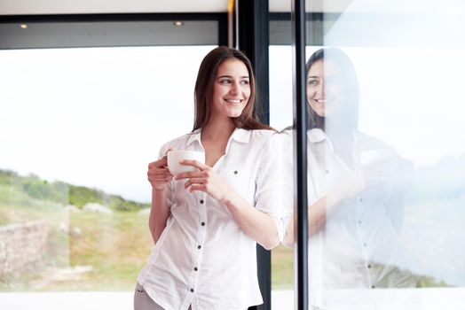 beautiful young woman drink first morning coffee at modern home interior with rain drops on big window door glass