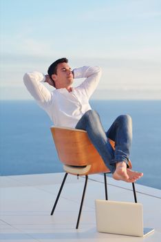 handsome young man relaxing and working on laptop computer at home balcony while looking sunset