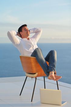 handsome young man relaxing and working on laptop computer at home balcony while looking sunset