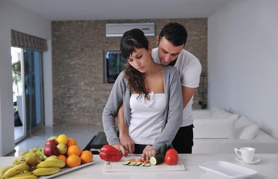 happy young couple have fun in  modern kitchen indoor  while preparing fresh fruits and vegetables food salad