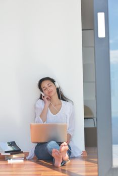 beautiful young woman relax and work on laptop computer while listening music on heaphones and read book at home