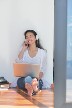 beautiful young woman relax and work on laptop computer while listening music on heaphones and read book at home