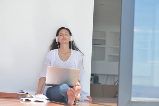 beautiful young woman relax and work on laptop computer while listening music on heaphones and read book at home