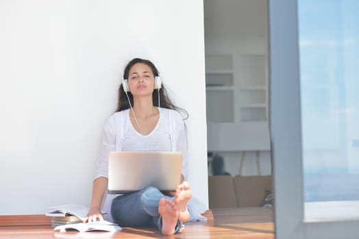 beautiful young woman relax and work on laptop computer while listening music on heaphones and read book at home