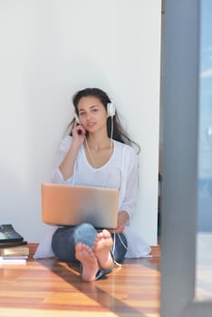 beautiful young woman relax and work on laptop computer while listening music on heaphones and read book at home