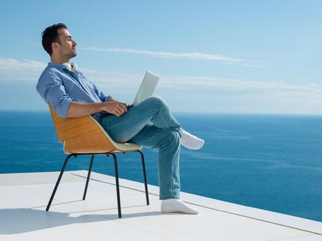 handsome young man relaxing and working on laptop computer at home balcony while looking sunset