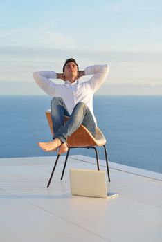 handsome young man relaxing and working on laptop computer at home balcony while looking sunset