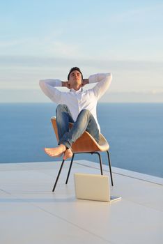 handsome young man relaxing and working on laptop computer at home balcony while looking sunset