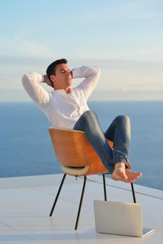 handsome young man relaxing and working on laptop computer at home balcony while looking sunset