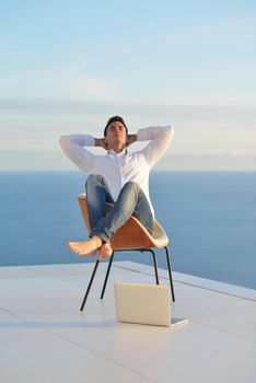 handsome young man relaxing and working on laptop computer at home balcony while looking sunset