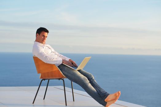 handsome young man relaxing and working on laptop computer at home balcony while looking sunset