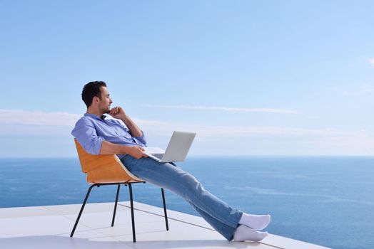 handsome young man relaxing and working on laptop computer at home balcony while looking sunset