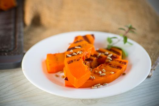 sweet baked grilled pumpkin with seeds in a plate on a wooden table
