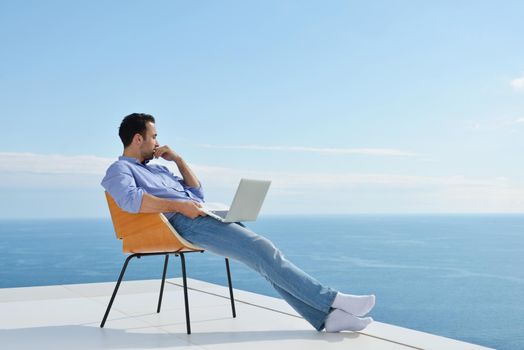 handsome young man relaxing and working on laptop computer at home balcony while looking sunset