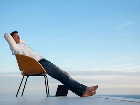 handsome young man relaxing and working on laptop computer at home balcony while looking sunset