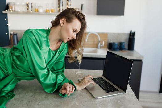 young smiling woman in dress working at home with laptop and champagne. High quality photo