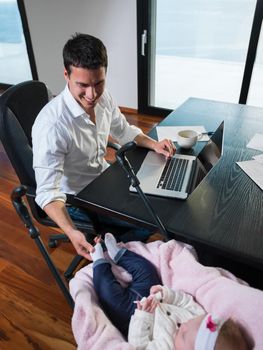 young man parent working on laptop computer at home office and take care of baby