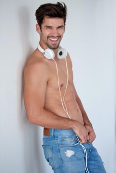 handsome young man listening music on headphones at modern home over  white wall and standing on hands