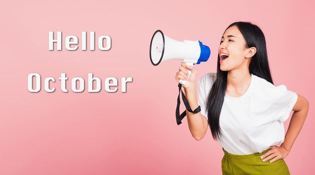 Hello October, Portrait of happy Asian beautiful young woman confident smiling face holding making announcement message shouting screaming in megaphone, studio shot isolated on pink background