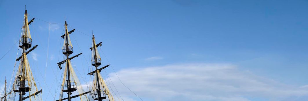 The masts of the old ship on the background of the blue sky. The concept of travel Copy space and banner