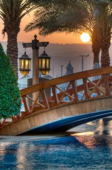 tropical sunset with bridge over hotel pool in foreground