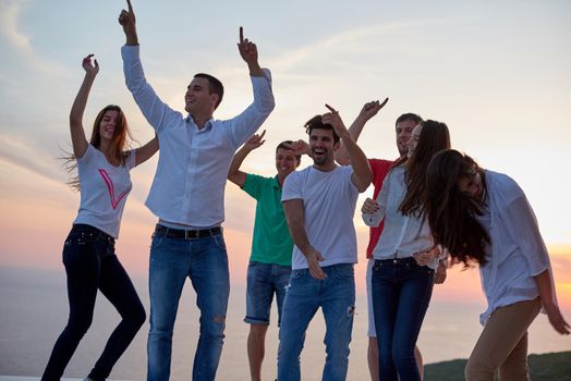 group of happy young people dancing and have fun on party in modern home bacony with sunset and ocean in background