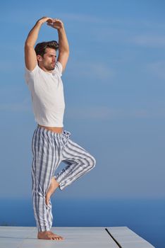 handsome young man practicing yoga on in modern home terace with ocean and sunset in background