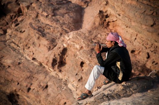 young jordanian  playing on his flute in the middle of petra mountains