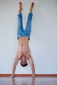 handsome young man listening music on headphones at modern home over  white wall and standing on hands