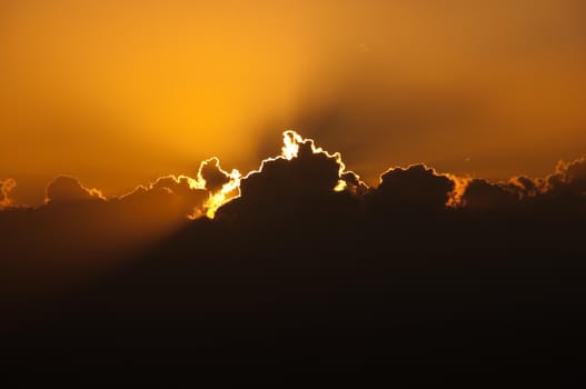 sun setting behind big cloud creating orange glow in the sky