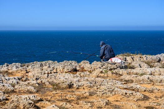 A lonesome fisherman is is sitting on the rocks and is catching his dinner with an huge fishing rod.